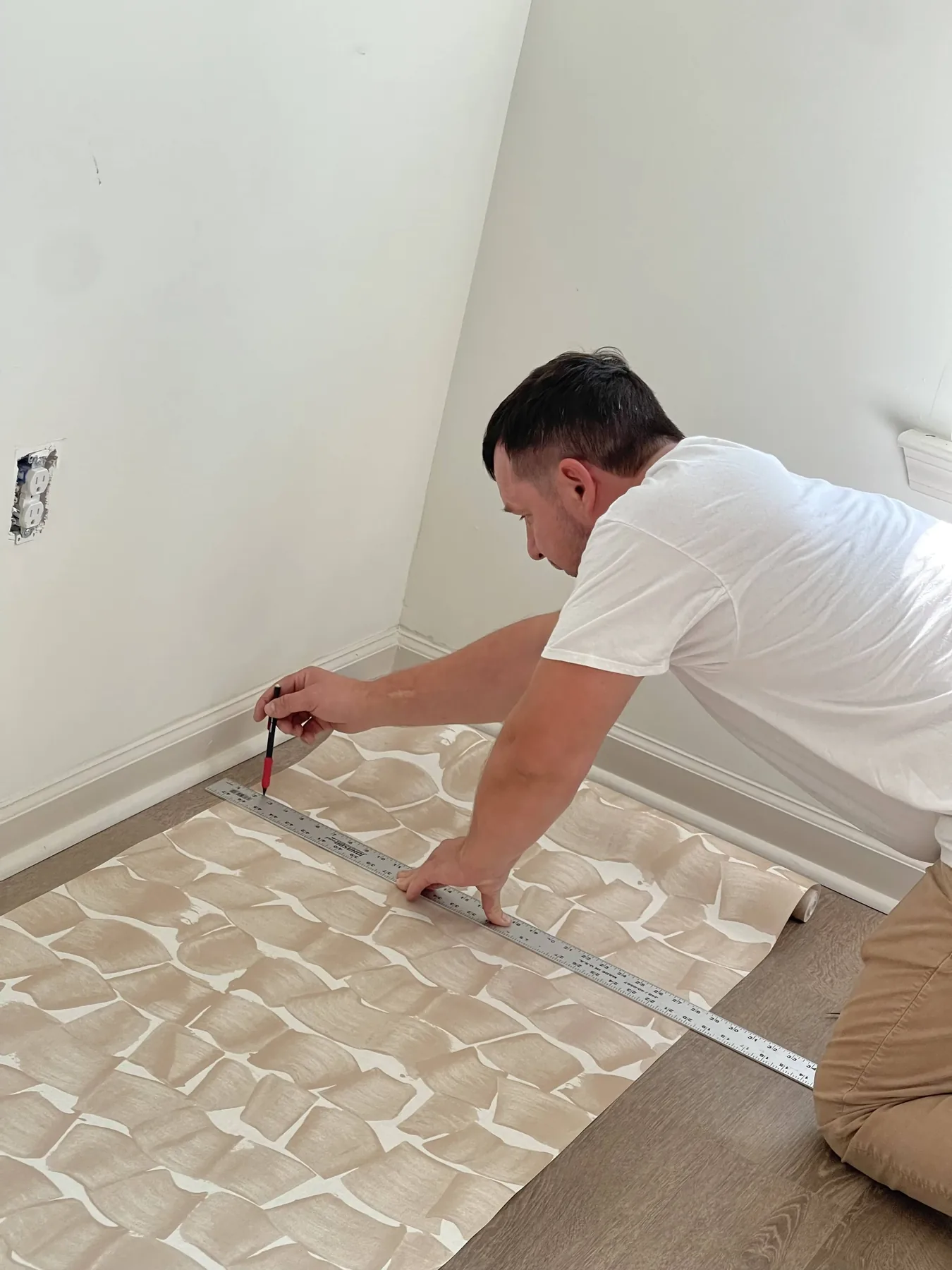 Installer measuring and cutting a roll of wallpaper on the floor